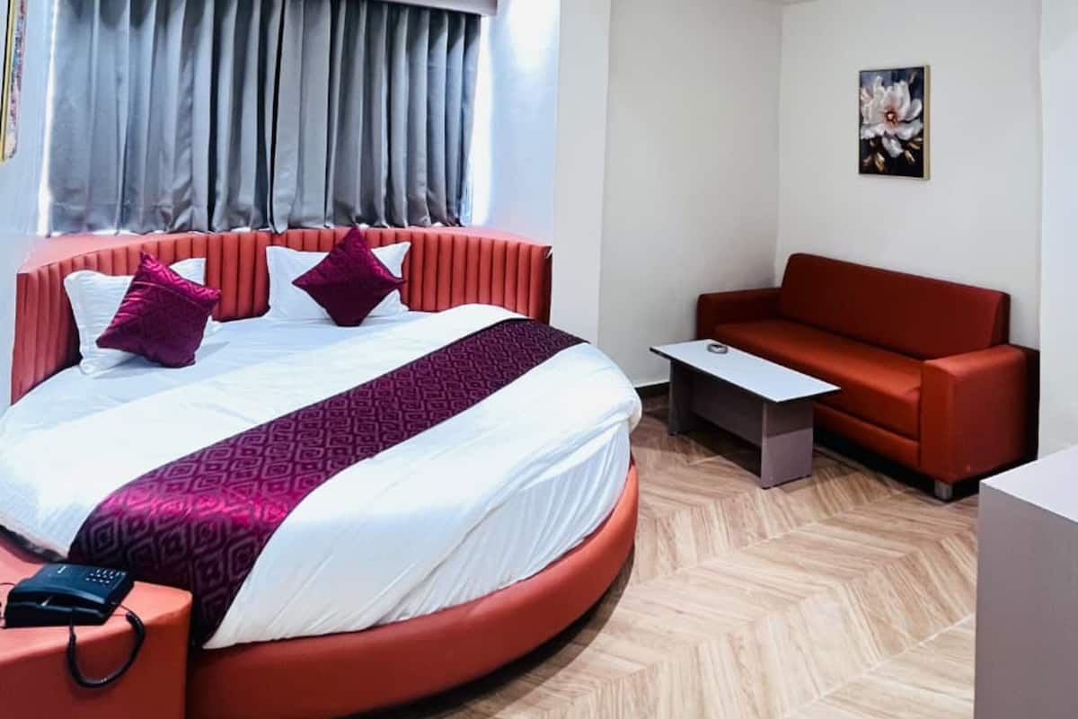 A modern hotel room with a circular bed, a red sofa, a small table, and a painting on the wall.