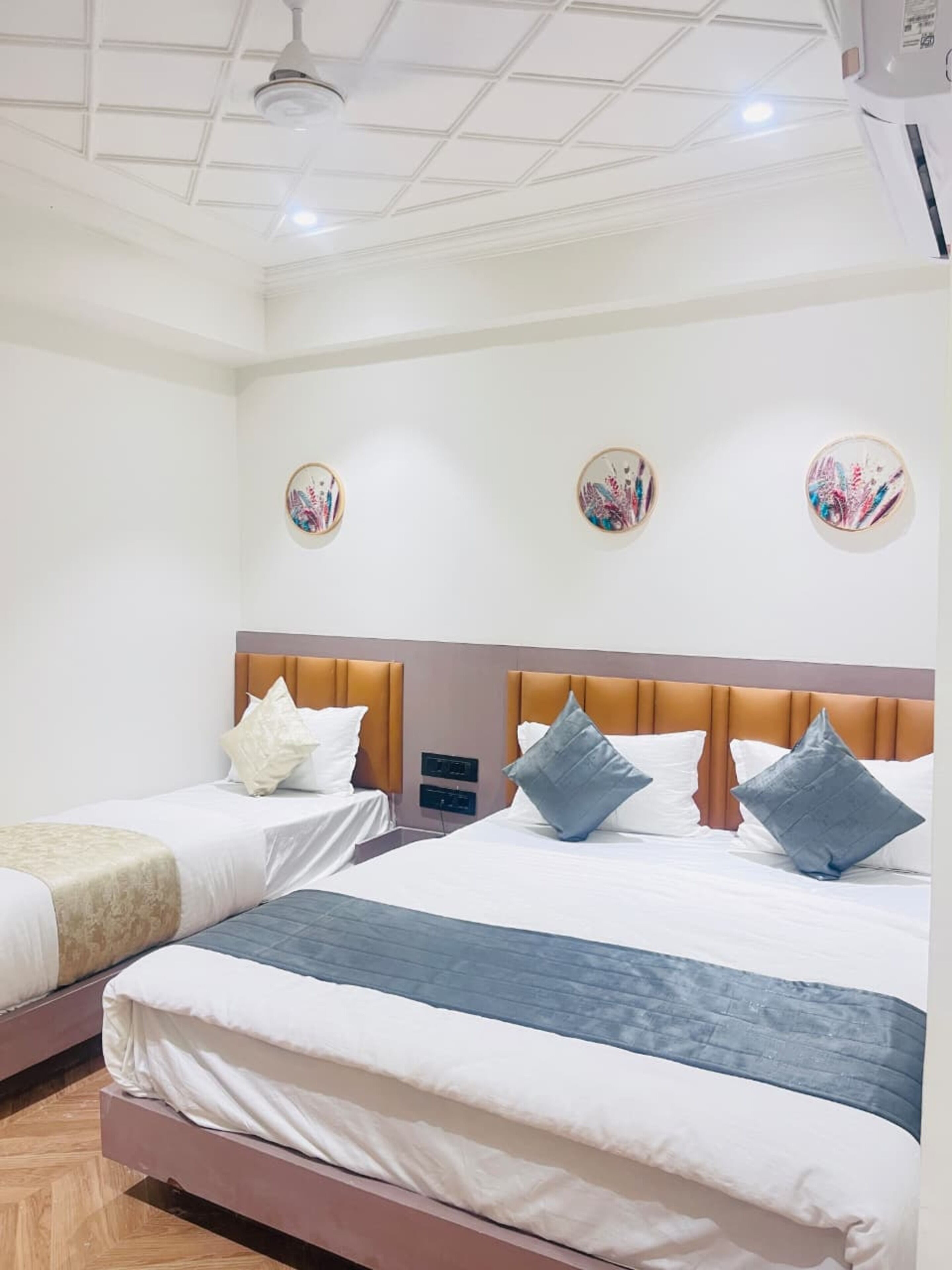 Habitación de hotel con dos camas, cada una con cabecera, ropa de cama blanca y almohadas decorativas. Hay luminarias fijadas a la pared y un ventilador de techo.