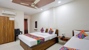 Une chambre d’hôtel avec un lit en bois, un bureau, une chaise, un ventilateur de plafond et un appareil de climatisation.