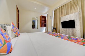 Una habitación de hotel con una cama grande, un televisor en la pared, un armario y una ventana con cortinas.