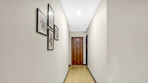 A hallway with a wooden door at the end, white walls, and framed pictures on the left wall. - Fabhotel Aditya Lodging (Chhatrapati Sambhajinagar)