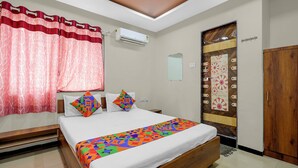 A bedroom with a bed, pillows, a mirror, an air conditioning unit, and a wooden door. - Fabhotel Aditya Lodging (Chhatrapati Sambhajinagar)