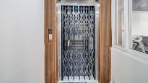 A narrow elevator with a wooden panel on the sides and a metal gate at the bottom. - Fabhotel High Rise Kokapet (Hyderabad)