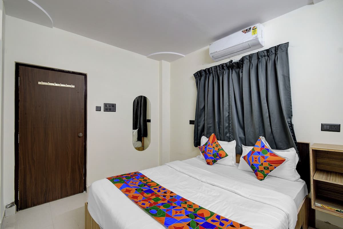 A hotel room with a bed, a wardrobe, a mirror, and an air conditioning unit.