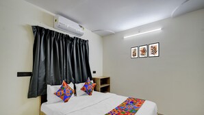 A neatly made bed with white bedding and colorful geometric pillows, a black curtain, and a wall-mounted air conditioner. - Fabhotel High Rise Kokapet (Hyderabad)