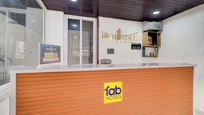 A hotel reception desk with a wooden counter, a reception area with a glass door, and a wall-mounted sign for the HighRise Hotel. - Fabhotel High Rise Kokapet (Hyderabad)