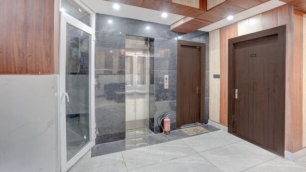 A modern interior with a glass door entrance, a fire extinguisher, and a wooden door. - Fabhotel Ivory Loft (Noida)