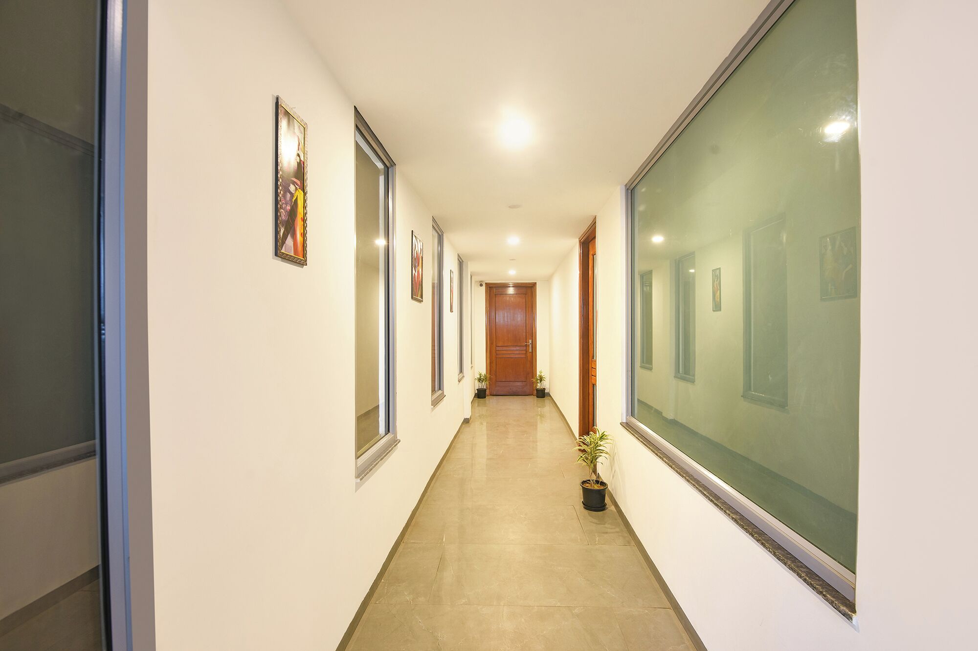 Un couloir orné de tableaux encadrés, avec une porte en bois et des plantes en pot.