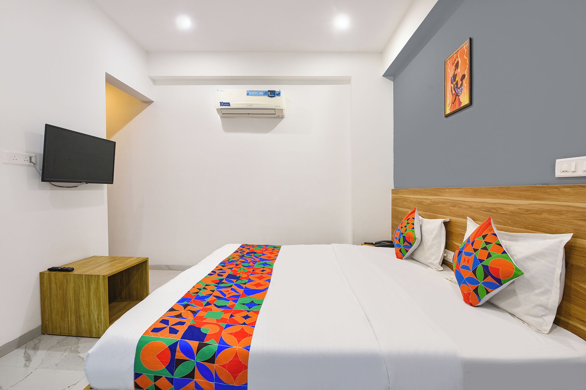 A hotel room with a bed, a TV, an air conditioner, and a painting on the wall.