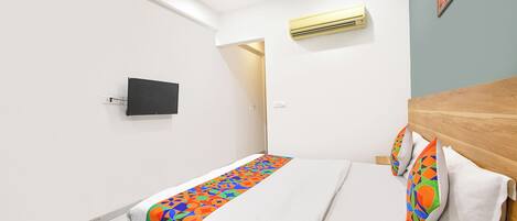 A modern hotel room with a bed, a flat-screen TV, an air conditioning unit, and a door leading to another room.