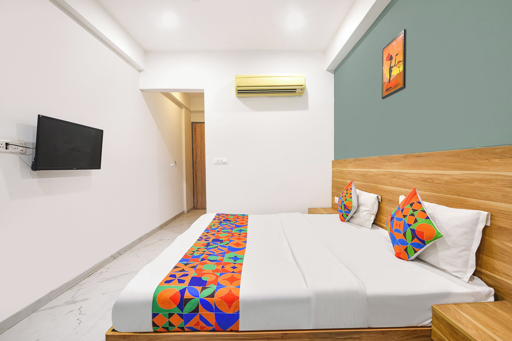 Ein Hotelzimmer mit Bett, Wandfernseher, Klimaanlage und einer Tür zu einem anderen Raum.