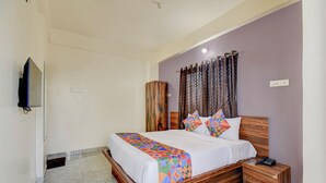 A bedroom with a wooden bed, a nightstand, a TV mounted on the wall, and a window with curtains. - Fabhotel Dream Sky (Pune)