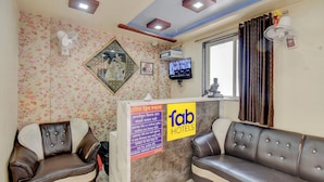 A hotel reception area with a floral wallpaper, a reception desk with a sign, a television, and two sofas. - Fabhotel Dream Sky (Pune)