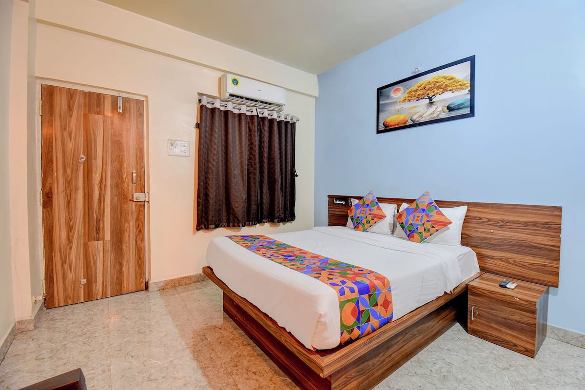 A bedroom with a wooden bed, a nightstand, a wall-mounted air conditioner, a door, and a window with curtains.