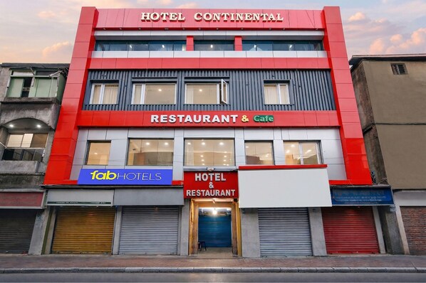 Un hôtel à la façade rouge et grise, avec un restaurant et un café au rez-de-chaussée, et une enseigne « fabHOTELS » sur le côté gauche.
