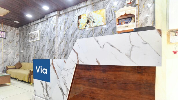 A reception area with marble walls, a wooden reception desk, a sofa, and a framed picture. - Fabhotel Mannat (Indore)