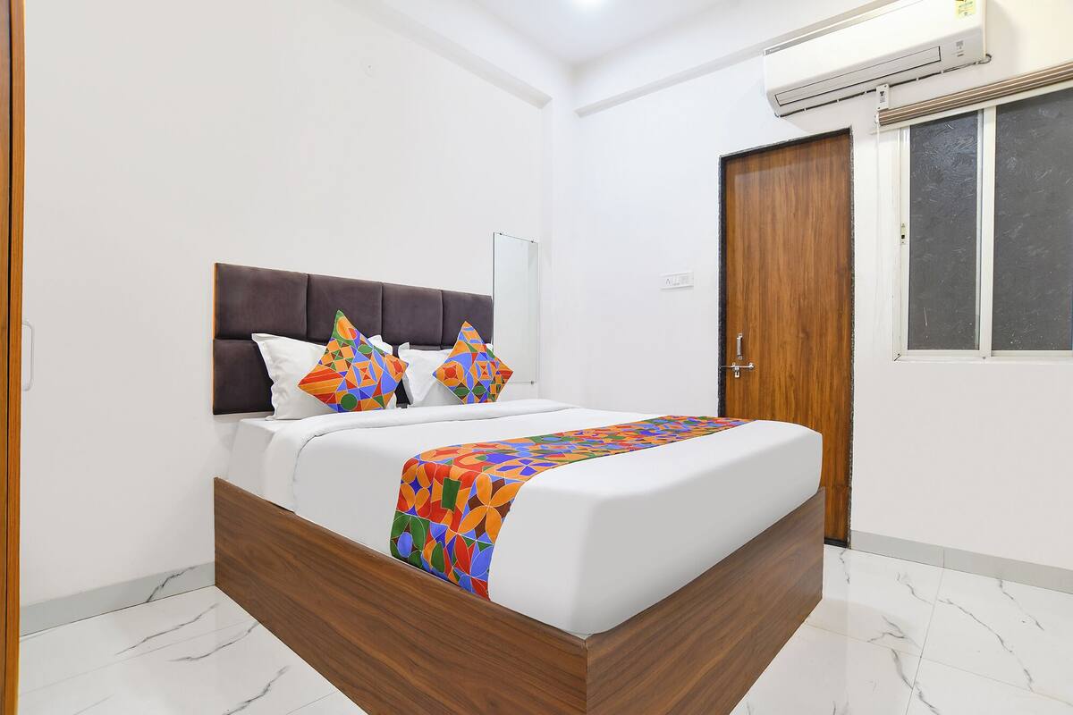 A bedroom with a wooden bed frame, white bedding, and colorful geometric pillows.