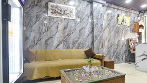 A room with a marble-patterned wall, a beige sofa, a glass coffee table with colorful objects, and a small plant. - Fabhotel Mannat (Indore)