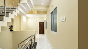 A modern hotel hallway with a marble floor, a metal staircase, and a fire extinguisher mounted on the wall. - Fabhotel Mannat (Indore)