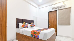 A bedroom with a wooden bed frame, white bedding, and colorful geometric pillows. - Fabhotel Mannat (Indore)