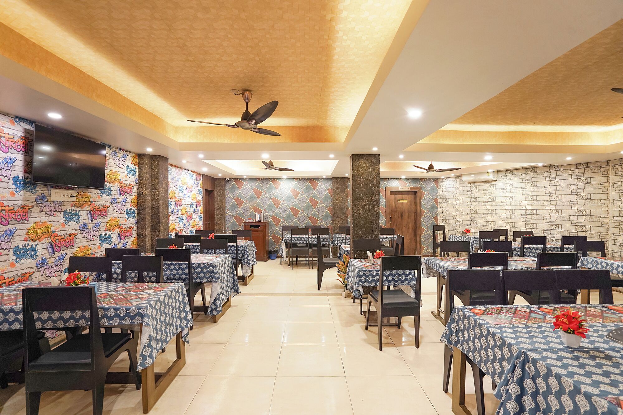 A restaurant with multiple tables and chairs, ceiling fans, and a patterned wall.