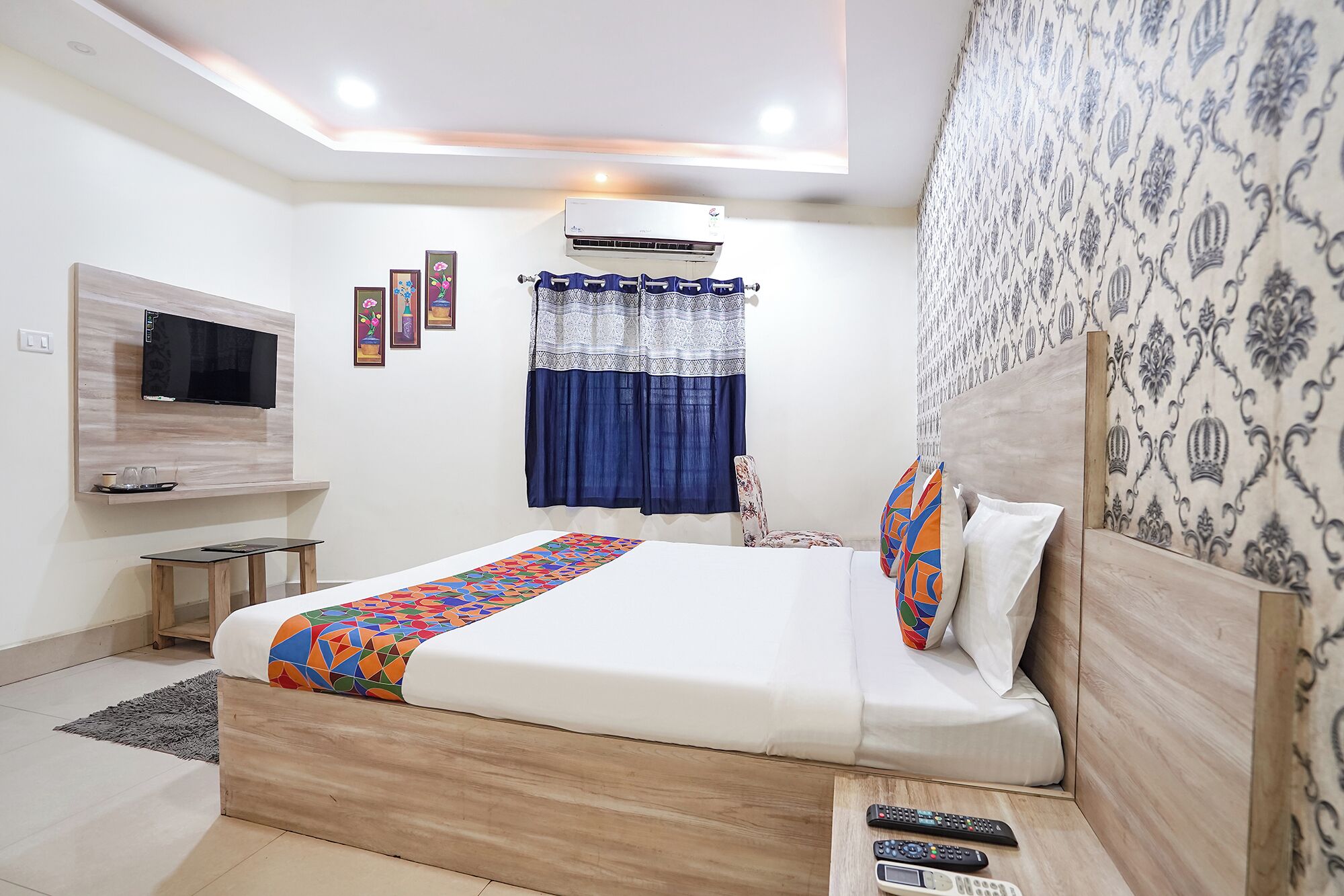 Une chambre moderne avec un lit, un téléviseur fixé au mur, un appareil de climatisation et un mur décoré d’un motif.