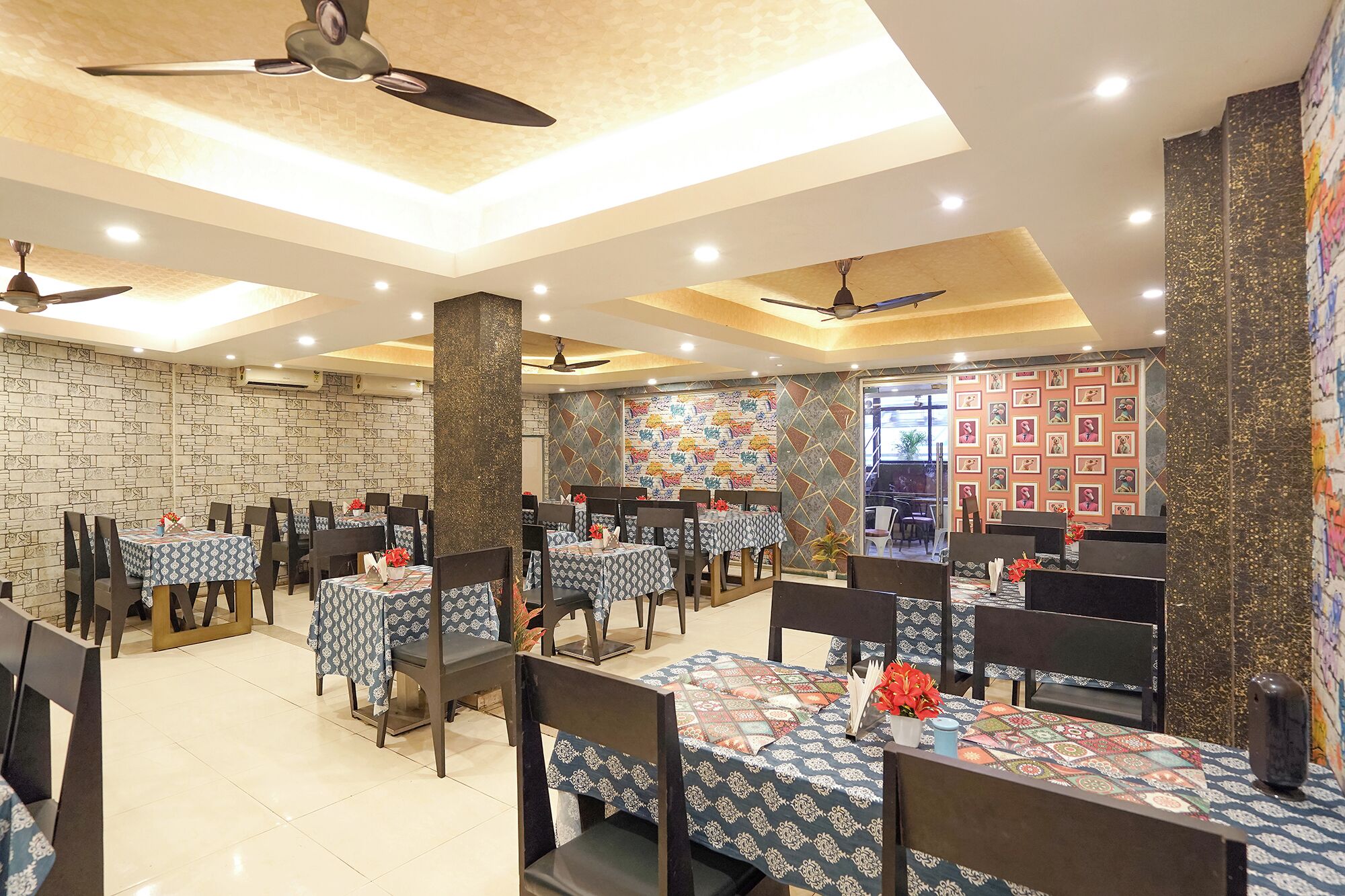 A restaurant with multiple tables and chairs, ceiling fans, and decorative wall patterns.