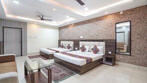 A modern hotel room with a large bed, two bedside tables, a glass coffee table, a sofa, a ceiling fan, and a large mirror. - Fabhotel Garden Tree (Bhubaneshwar)