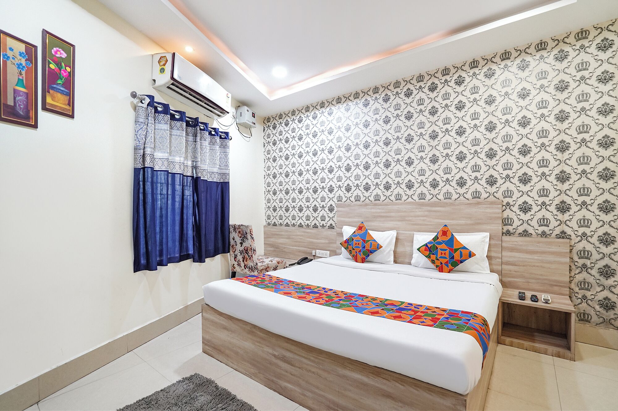 A bedroom with a bed, a nightstand, a wall-mounted air conditioner, and patterned wallpaper.