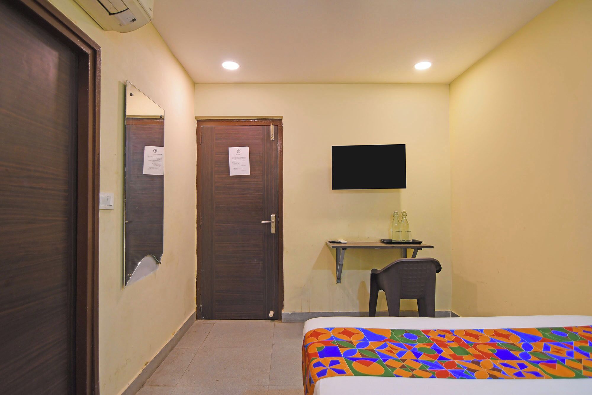 A hotel room with a bed, a desk with a chair, a television, and a door.