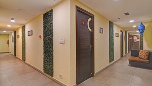 Corridoio di un hotel con una porta in legno, pannelli verticali verdi e un'area relax con un cuscino decorato.