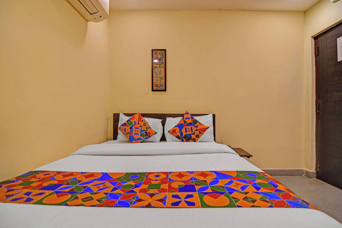 Un dormitorio con cama, dos almohadas, una colcha colorida, un aire acondicionado de pared y una puerta.