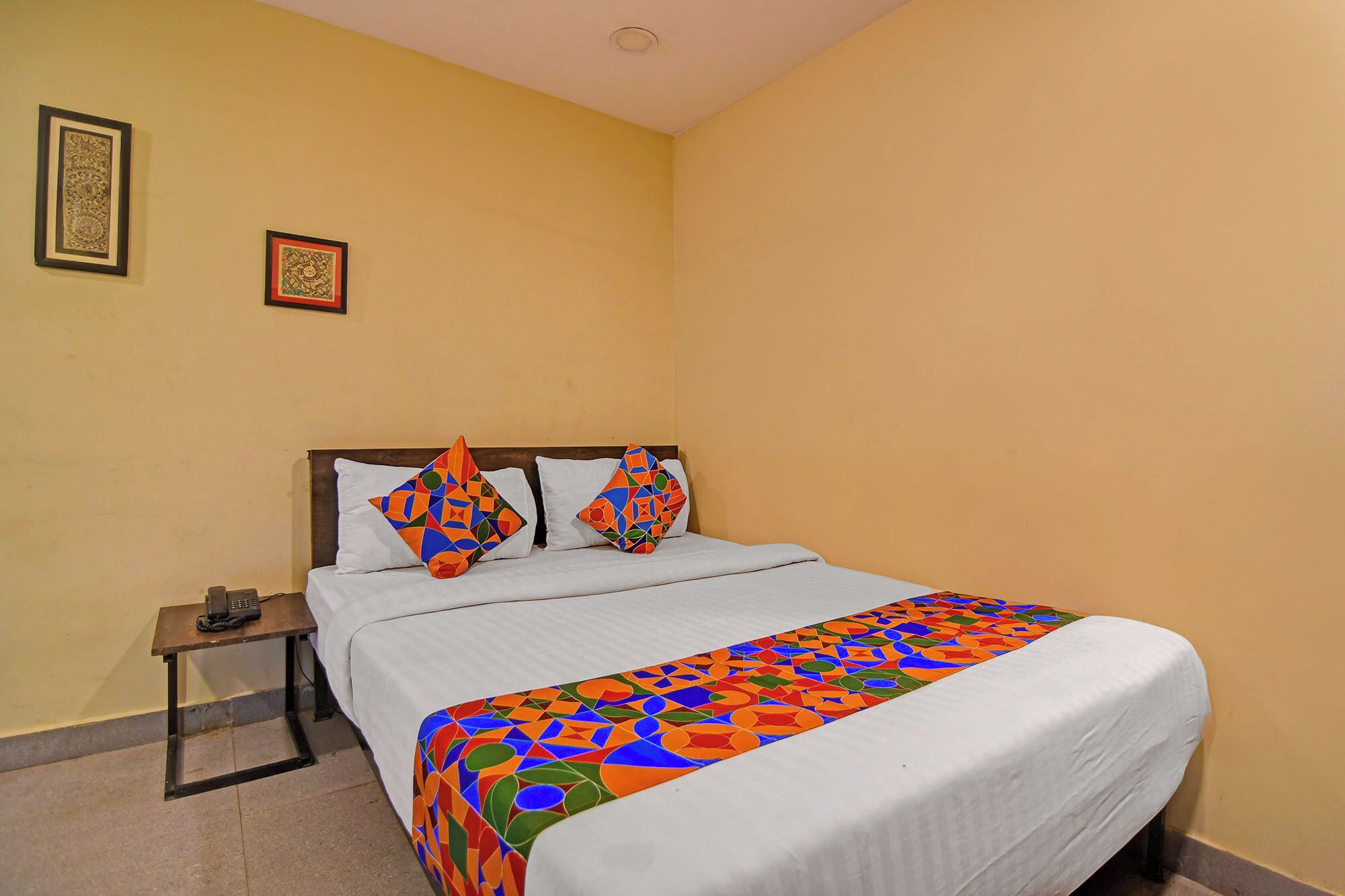 Habitación de hotel con una cama, una mesita de noche y dos cuadros en la pared.