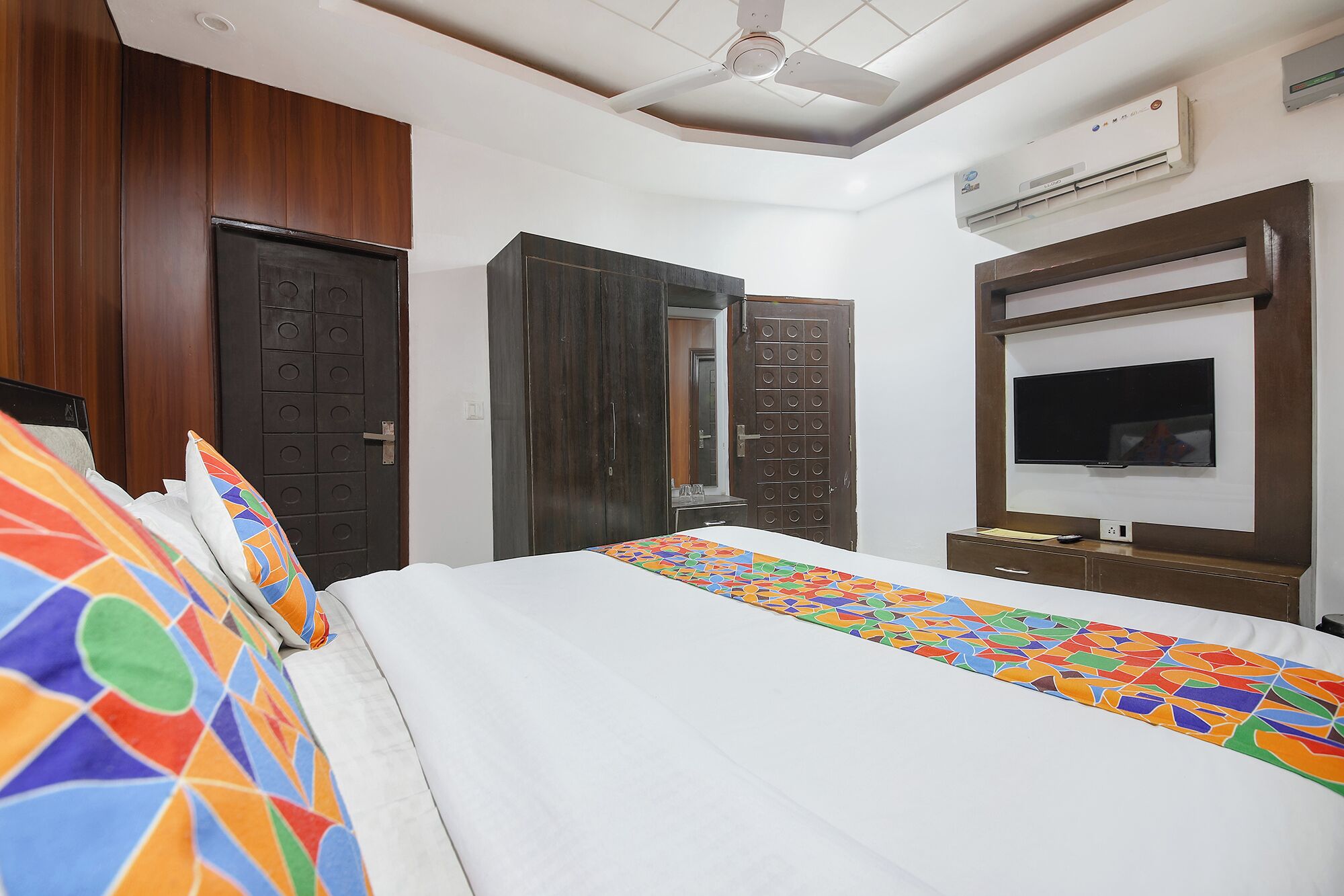 A hotel room with a bed, a TV, a wardrobe, and a ceiling fan.