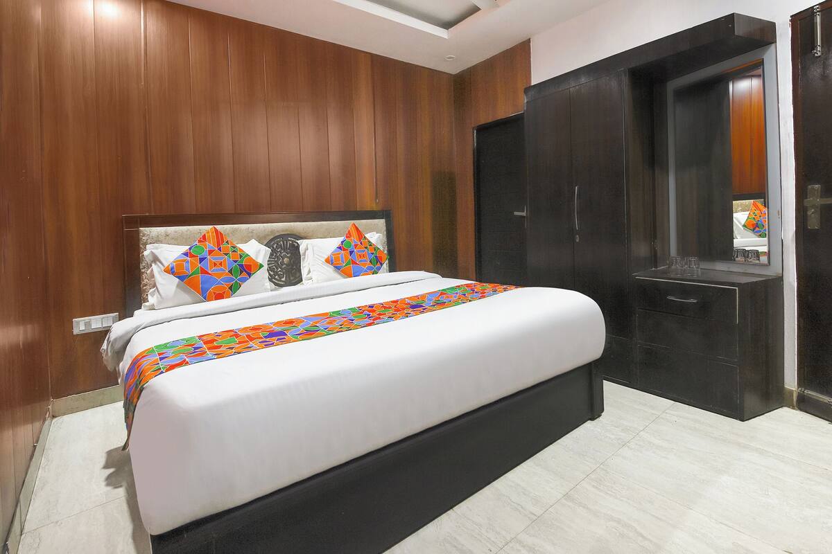 Une chambre d’hôtel moderne avec un grand lit, des murs recouverts de panneaux en bois, une porte sombre et un petit espace salle de bain.