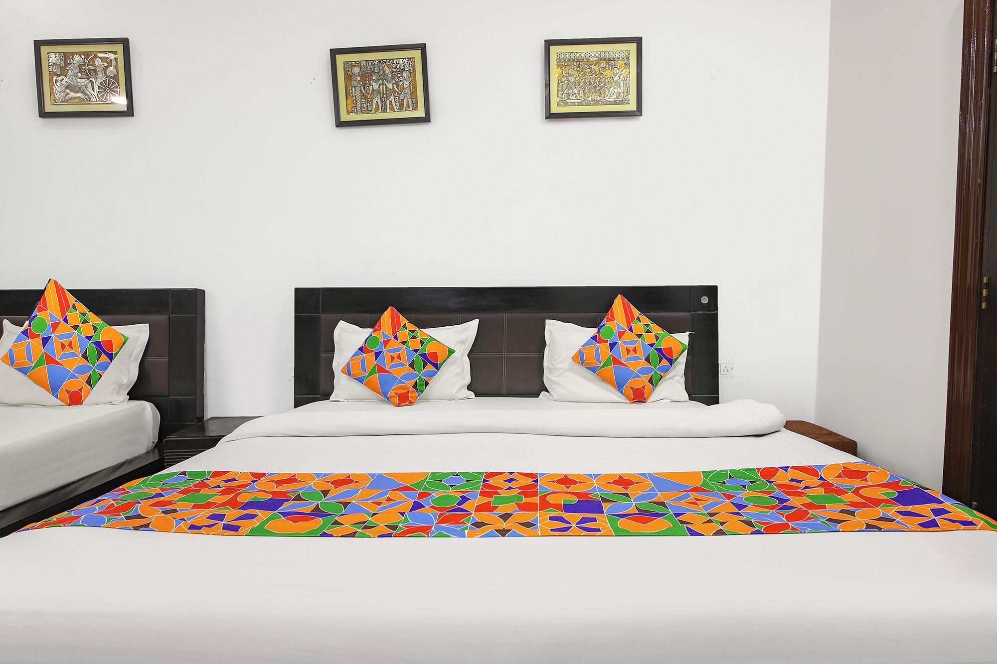 Habitación de hotel con una cama grande, dos almohadas, un cabecero y tres obras de arte enmarcadas en la pared.