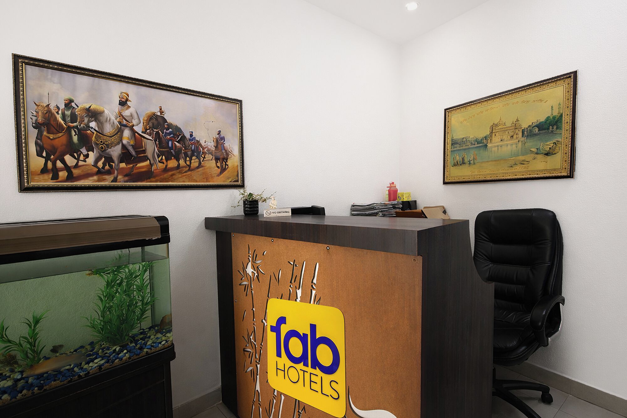 Uma mesa de recepção com a placa 'Fab Hotels', uma pintura histórica emoldurada e um aquário.