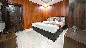 Una habitación de hotel con cama, una puerta de madera, un escritorio y un ventilador de techo.