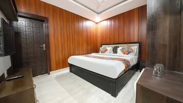 Een hotelkamer met een bed, een houten deur, een bureau en een plafondventilator.