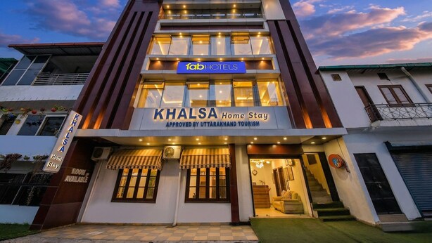 Un edificio de varios pisos con un cartel que indica 'KHALSA Home Stay' y 'fabHOTELS'.