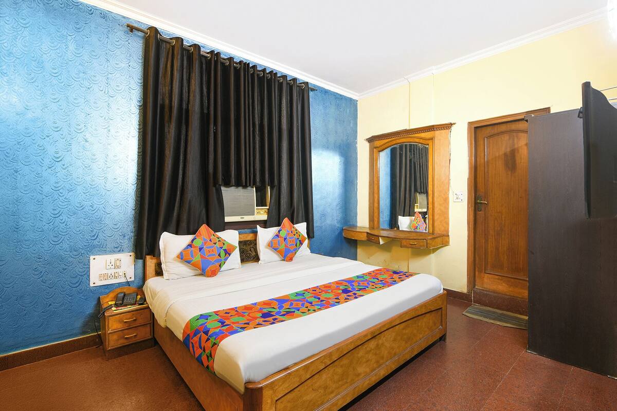 A hotel room with a bed, a wooden wardrobe, a mirror, and a nightstand with a telephone.