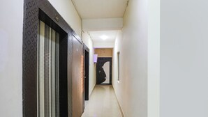 A hallway with a patterned door, a window, and a door with a number plate. - Fabhotel Arka Residency (Jaipur)