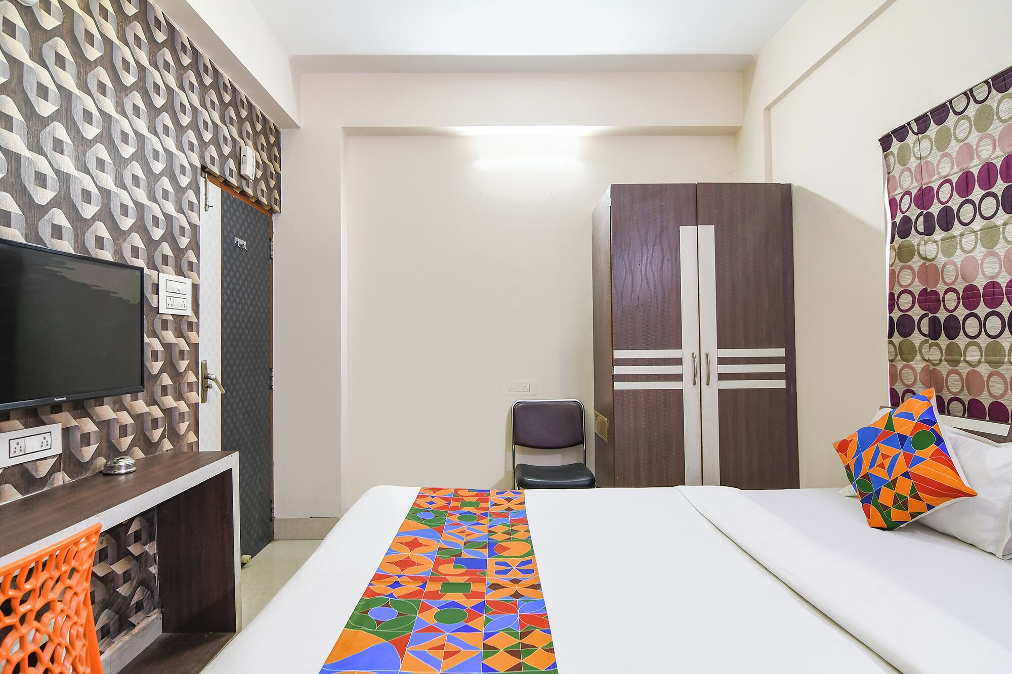 A hotel room with a bed, a TV, a wardrobe, and a patterned wall.