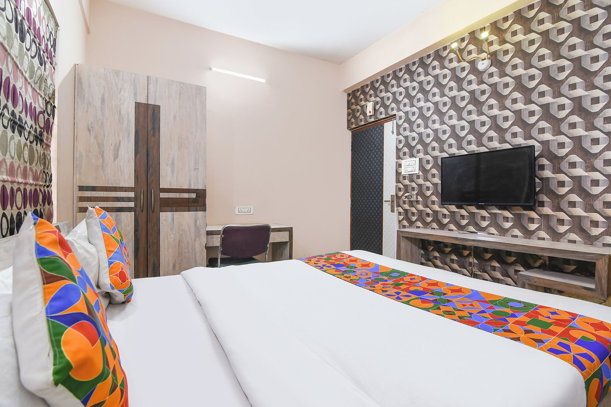 Une chambre d’hôtel équipée d’un lit, d’un bureau et d’un téléviseur fixé au mur.