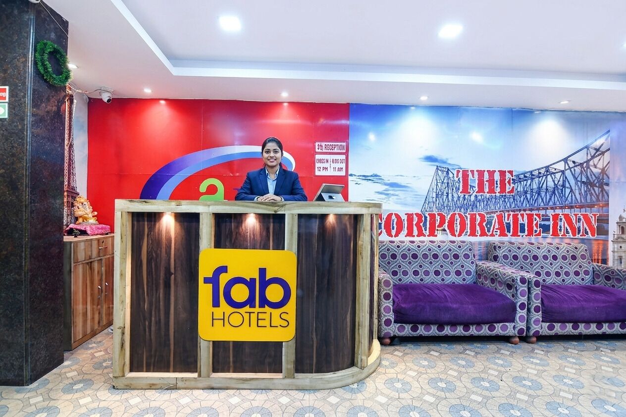 Un comptoir d’accueil avec une enseigne « Fab Hotels », un mur rouge orné d’un logo circulaire et une grande bannière sur laquelle on peut lire « THE CORPORATE INN ».