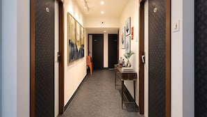 A hallway with doors, artwork, a small table with a vase, and a chair. - Fabhotel The Corporate Inn I (Kolkata)