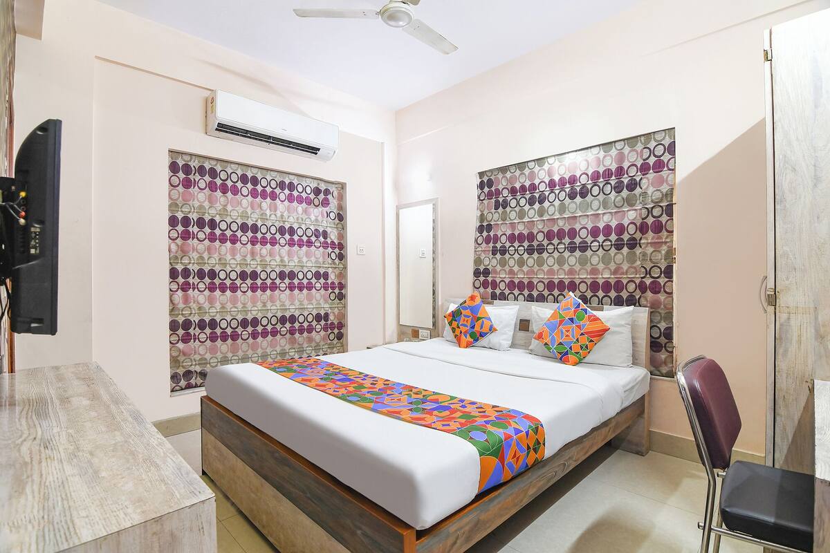 A bedroom with a bed, a chair, a TV, and an air conditioning unit.
