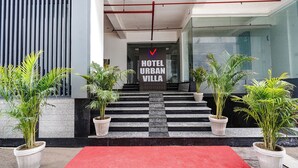 Entrada de un hotel con alfombra roja, plantas en macetas y un cartel que dice 'HOTEL URBAN VILLA'.