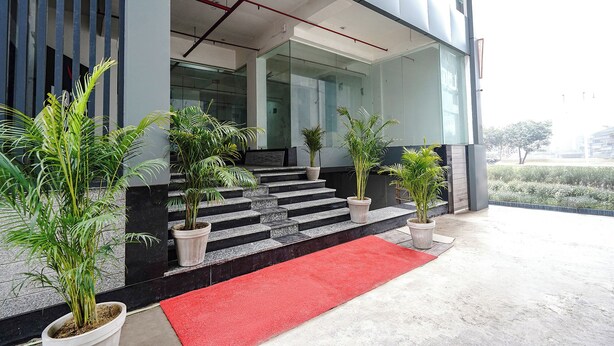 Una entrada de edificio moderna con alfombra roja, plantas en macetas y una escalera que lleva a la entrada.