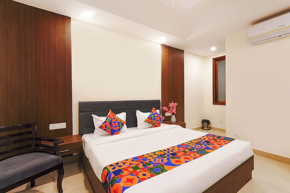 Habitación de hotel con cama, una silla, mesita de noche, un jarrón con flores y un equipo de aire acondicionado.
